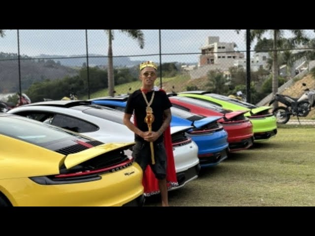 Homem com coroa e cetro ao lado de vários Porsches 911 coloridos